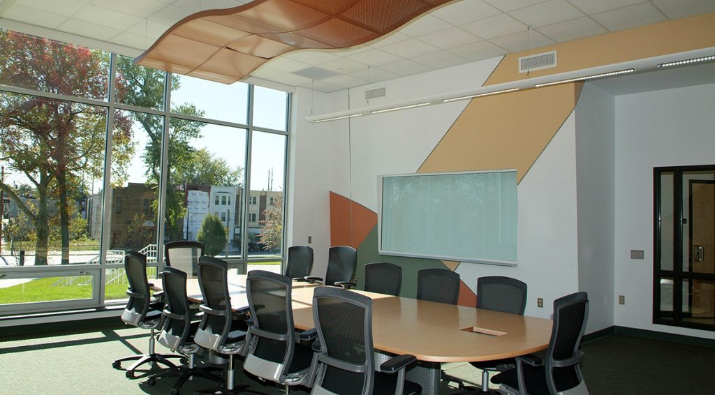 A conference room with an oval table, chairs pushed in all around, and a wall of windows behind the table